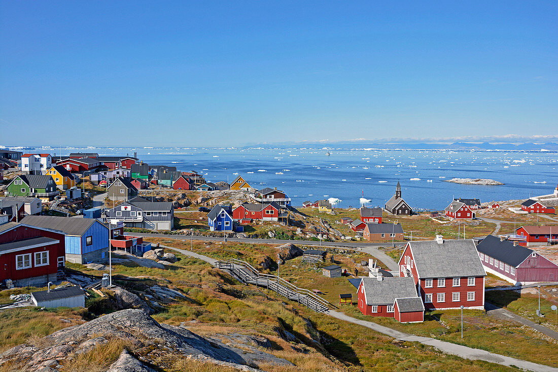 Disco bay; West Greenland; brightly painted wooden houses by Ilulissat; View of the Disko Bay; floating ice floes; mountainous terrain; Mountain range in the background; blue sky and sunshine