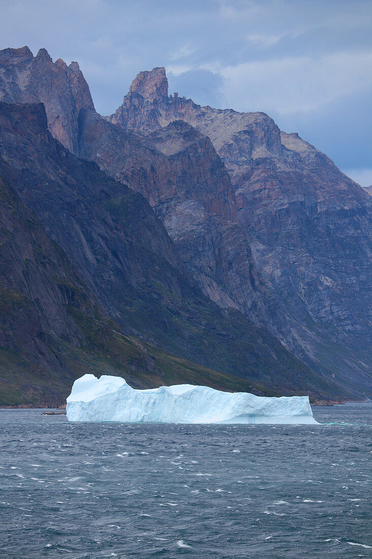 Prins Christian Sund in South Greenland; Passage at the southern tip; Iceberg block swims towards the open sea; steep, rocky mountain slopes line the waterway; bad weather and dark gray rain clouds