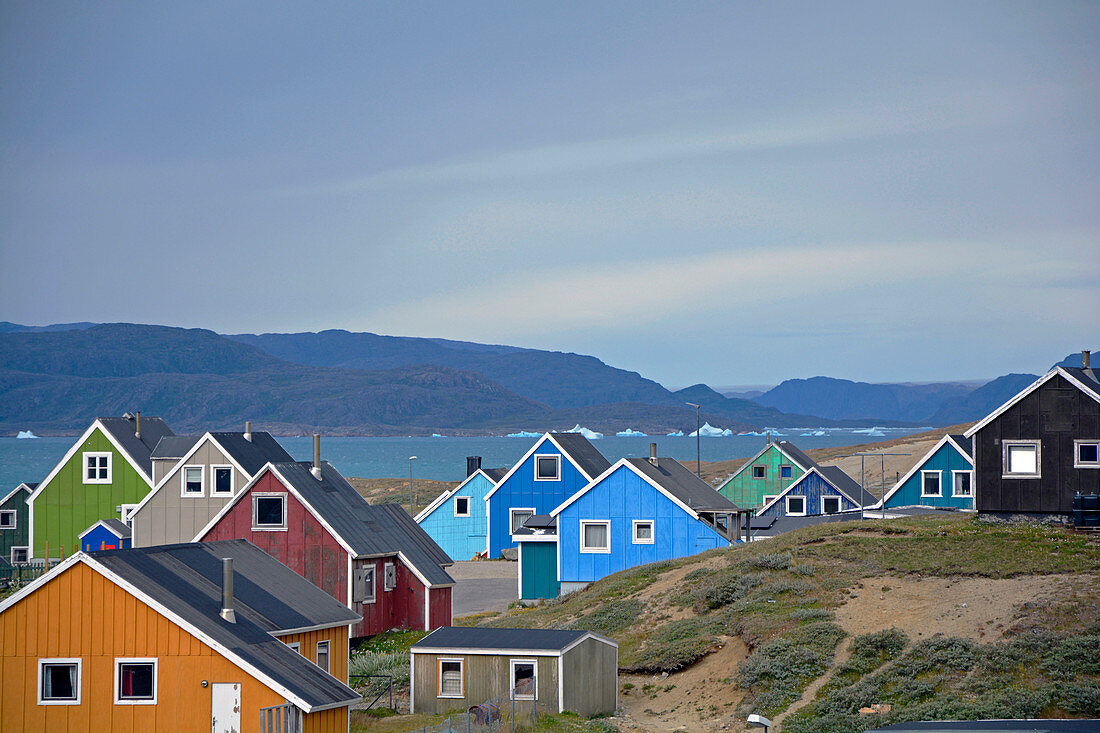 Narsaq, typische, bunt angestrichene Holzhäuser mit Blick auf Bucht und Eisberge, Südgrönland, Grönland