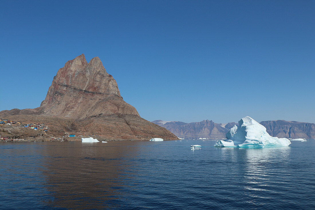 Iceberg in front of Uummannaq; Island in West Greenland; &quot;uummannaq&quot; means the &quot;seal-shaped&quot; and refers to the shape of the mountain; below the mountain are the colorful wooden houses in the hills; an iceberg and numerous ice floes float off the island;