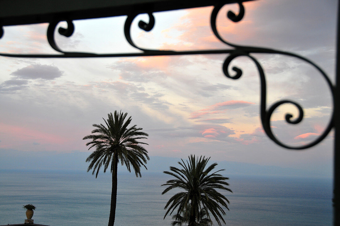 Sonnenuntergang mit Palmen und Gitter und Meer, Taormina, Ostküste, Sizilien, Italien
