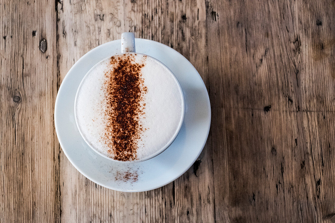 A cup of coffee in a cafe, a cappuchino with frothy top and sprinkled chocolate powder.
