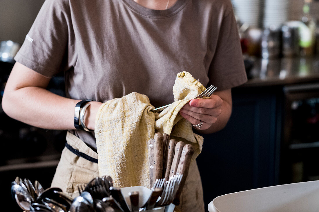 A staff member drying cutlery in a cafe.