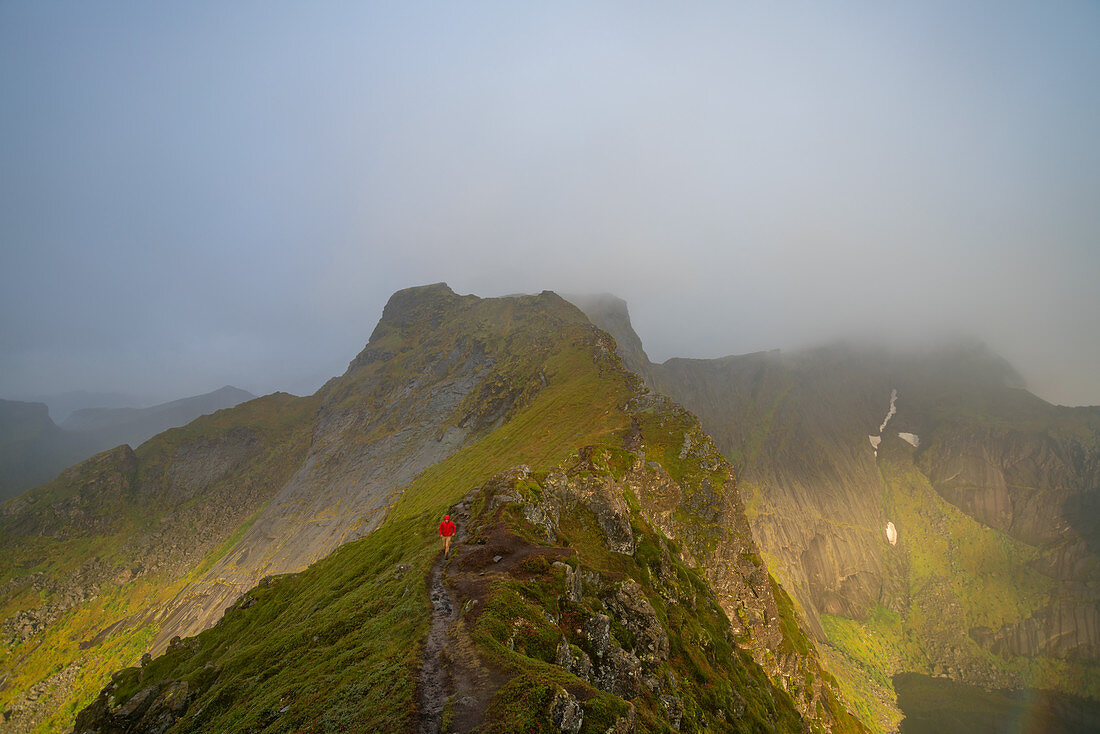 Wanderer in den Bergen mit Wolken, die von den Gipfeln auf der Insel Senja, Bezirk Troms, herabschweben