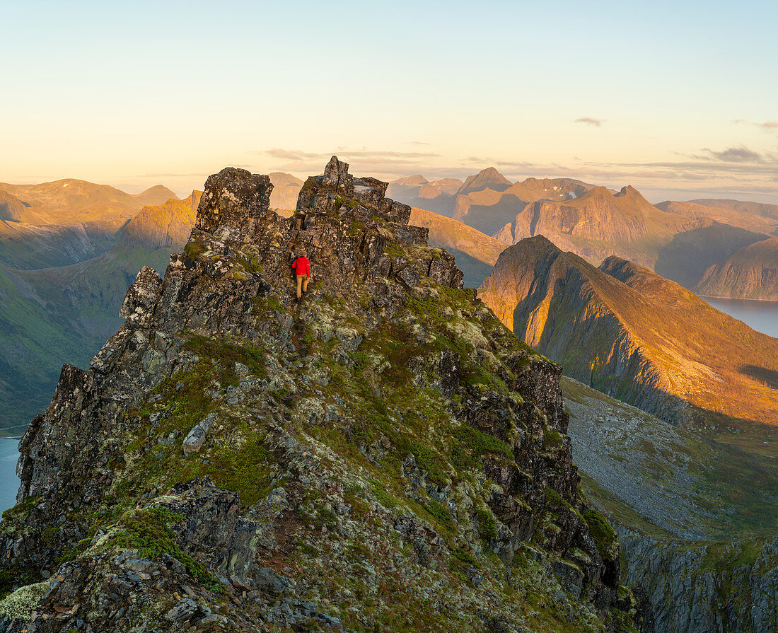 Man climbing up a steep peak in the jagged landscape of Senja Island, Troms