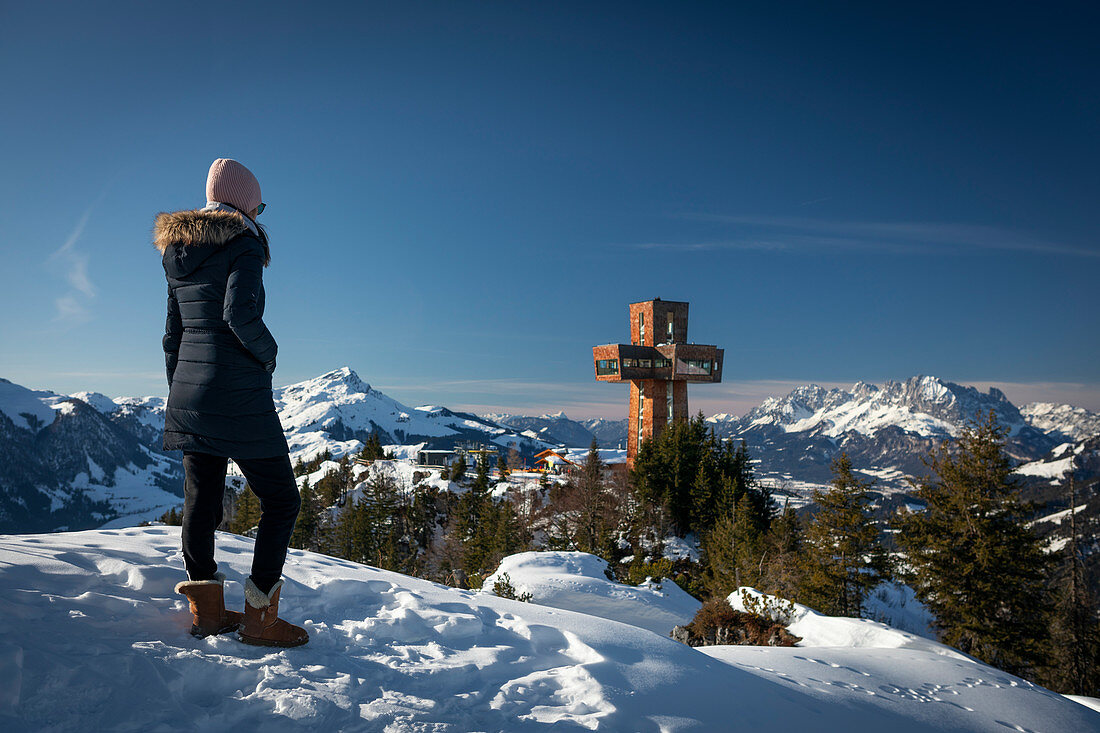 Frau mit Mantel und Mütze mit Blick auf Jakobskreuz und Ellmauer Halt in Fieberbrunn Wilder Kaiser, Winter in Tirol, Österreich