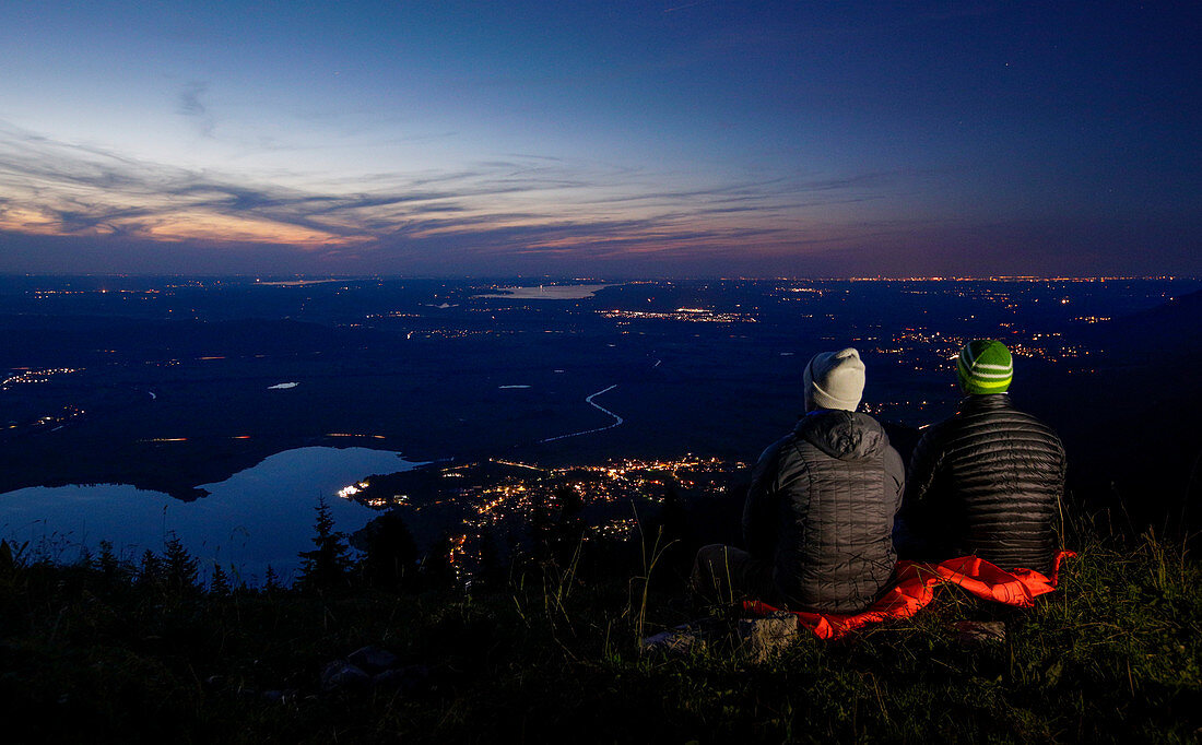Hikers sit on Jochberg overlooking Kochelsee from above after sunset, Bavaria