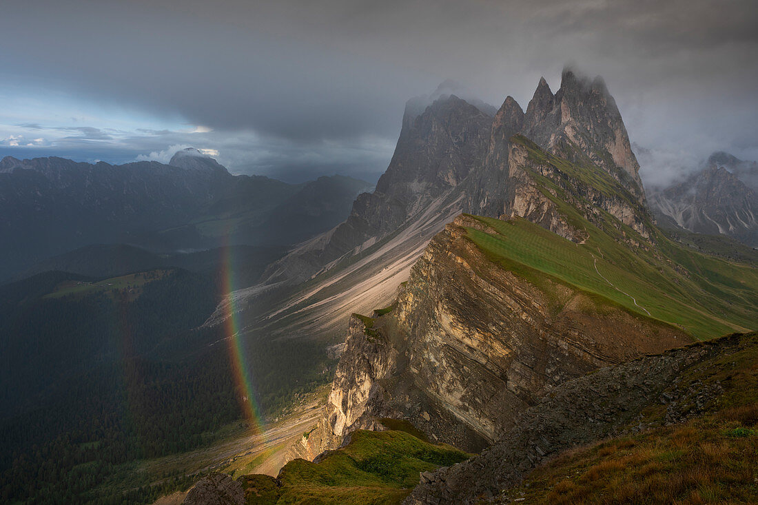 Seceda mountainside with thick clouds, sun and rainbow in the Dolomites near Ortisei, South Tyrol
