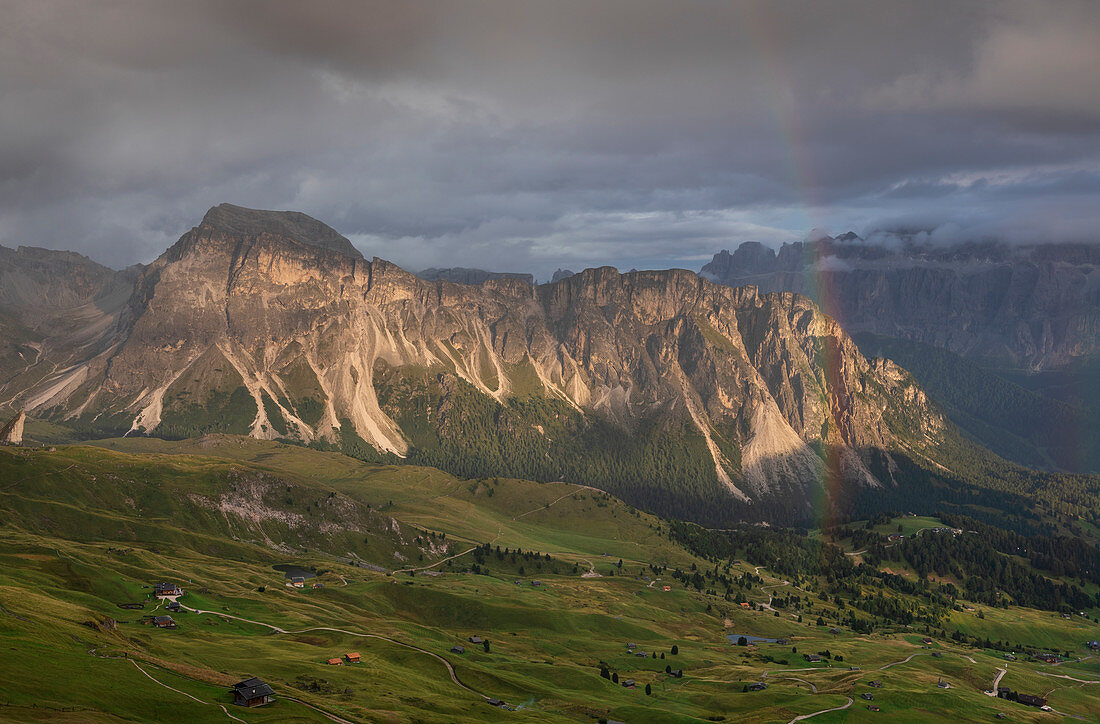 Gebirgsflanke bei Seceda mit dichten Wolken, Sonne und Regenbogen in den Dolomiten bei St. Ulrich, Südtirol