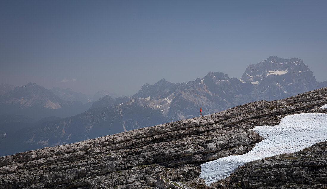 Frau wandert über Felskante, Gebirge der Dolomiten im Hintergrund, mit Schneefeld, Cinque Torri Südtirol