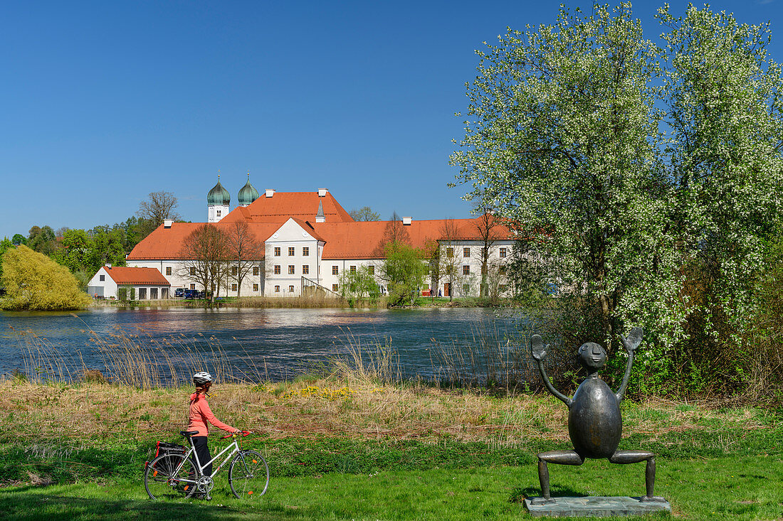 Woman cycling in front of Klostersee and Kloster Seeon, Kloster Seeon, Benediktradweg, Chiemgau, Upper Bavaria, Bavaria, Germany