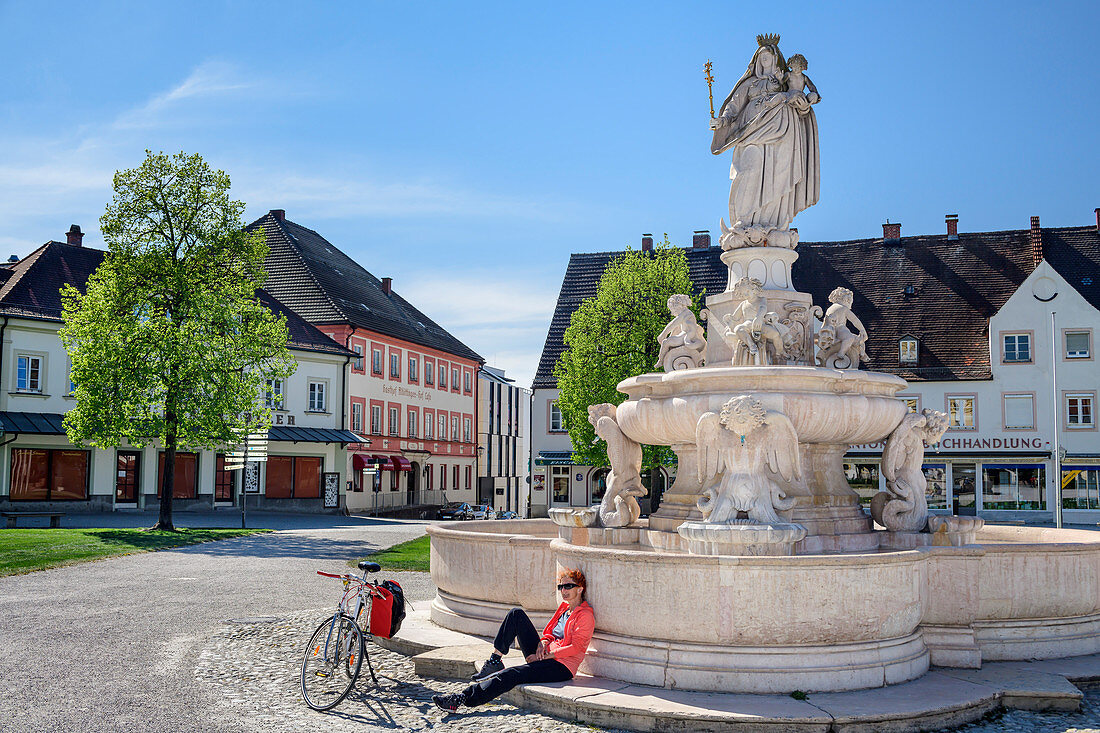 Woman cycling sits at fountain and takes a break, Altötting, Benediktradweg, Upper Bavaria, Bavaria, Germany