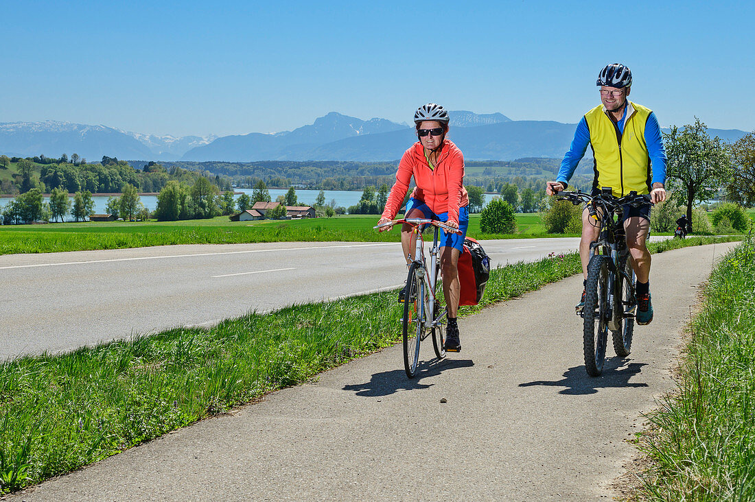 Woman and man cycling, Tachinger See and Chiemgau Alps in the background, Tachinger See, Benediktradweg, Upper Bavaria, Bavaria, Germany