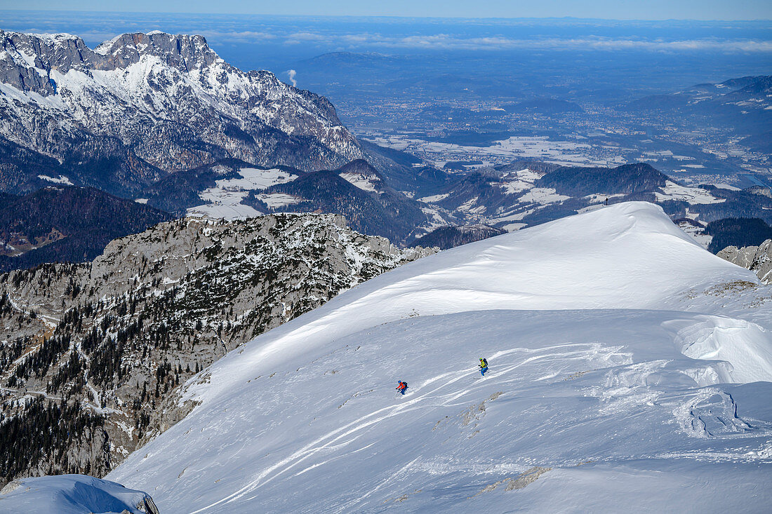 Zwei Personen auf Skitour fahren Schneeflanke hinab, Untersberg im Hintergrund, Hohes Brett, Nationalpark Berchtesgaden, Berchtesgadener Alpen, Oberbayern, Bayern, Deutschland