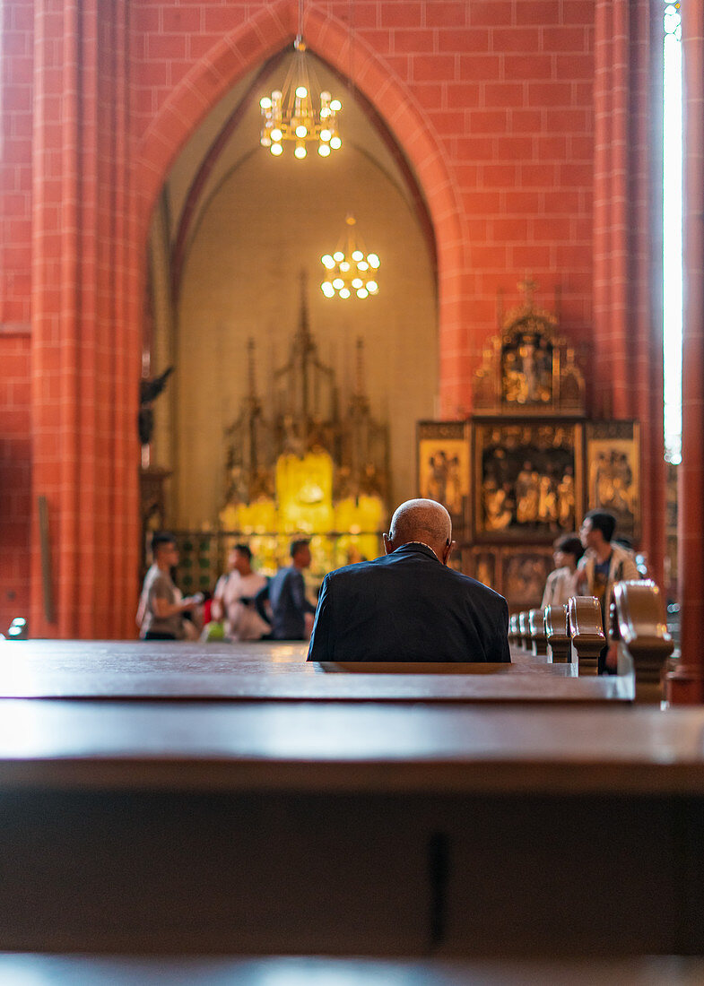 Mann betet im Kaiserdom St. Bartholomäus in Frankfurt am Main, Deutschland