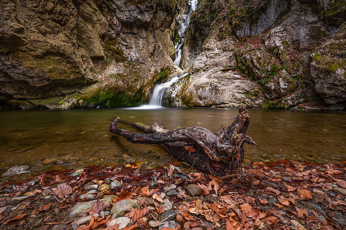Ein kleiner Wasserfall mit einem Baumstamm in Vordergrund in der Kesselfallklamm in Semriach, Österreich