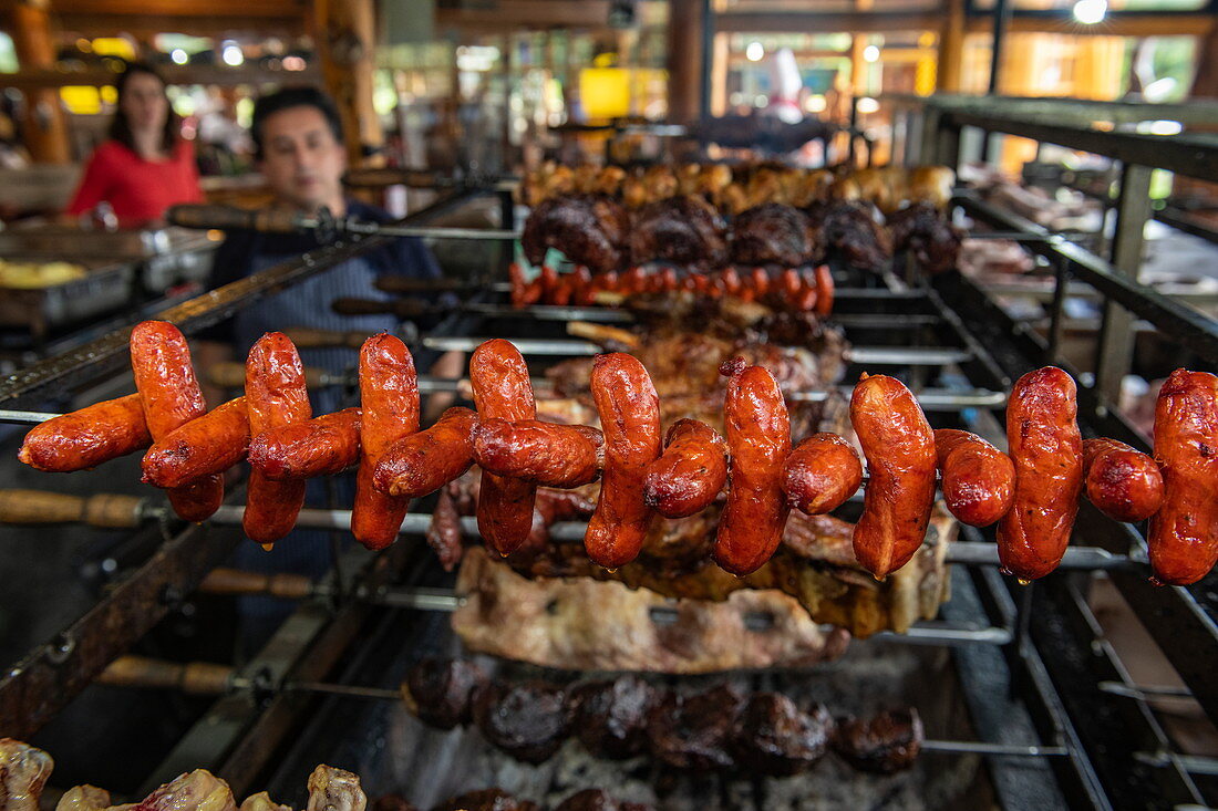 Sausages (chorizo) and other meat are grilled on rotating skewers in a restaurant, Puerto Montt, Los Lagos, Patagonia, Chile, South America