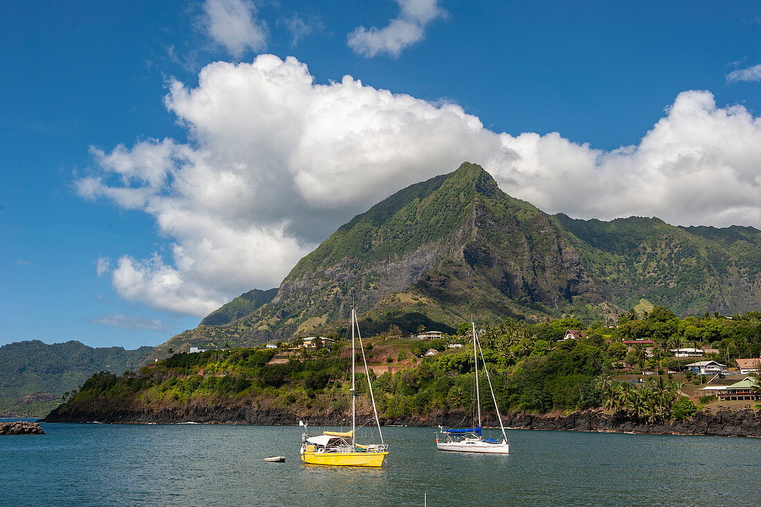 Two sailing boats are moored in the sun in front of a massive mountain, Atuona, Hiva Oa, Marquesas Islands, French Polynesia, South Pacific