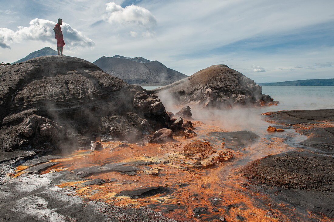 Mann steht auf Felsen und betrachtet Vulkanlandschaft mit orangefarbener Erde und heißen Quellen in der Nähe eines aktiven Vulkans, Rabaul, Provinz Ost-New Britain, Papua-Neuguinea, Südpazifik