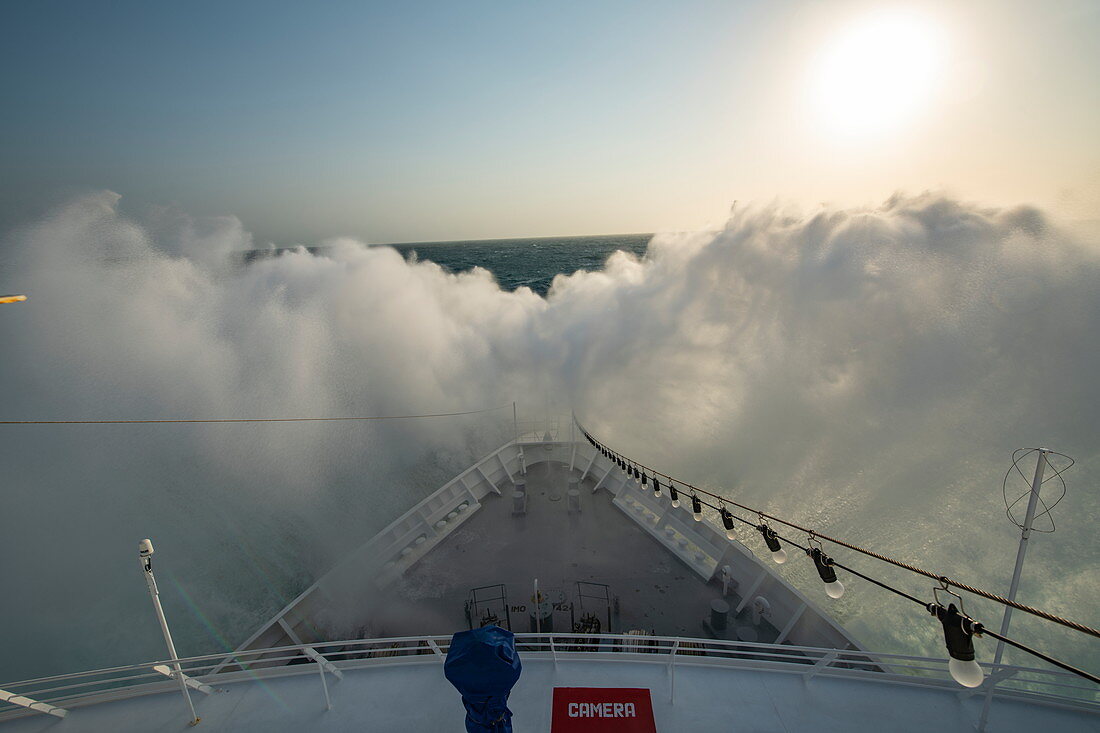 The front of an expedition cruise ship encounters a large wave and sends spray high above the bow at sea in the Caribbean, near Colombia