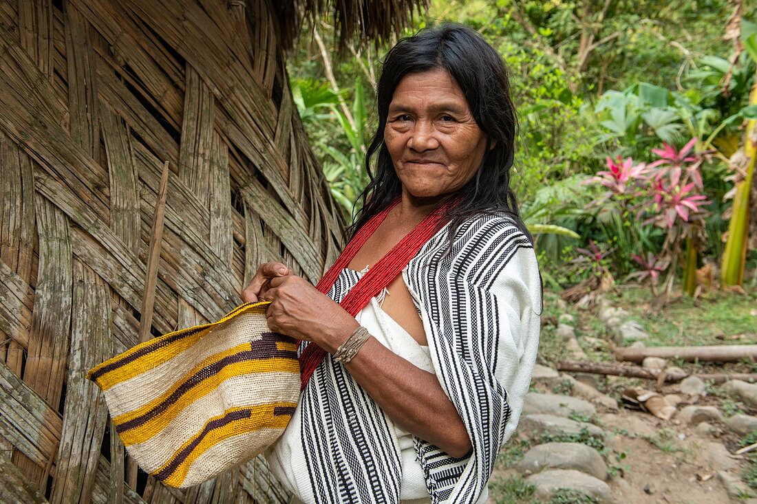 A woman holding a handmade basket is standing next to her hut, Santa Marta, Magdalena, Colombia, Caribbean