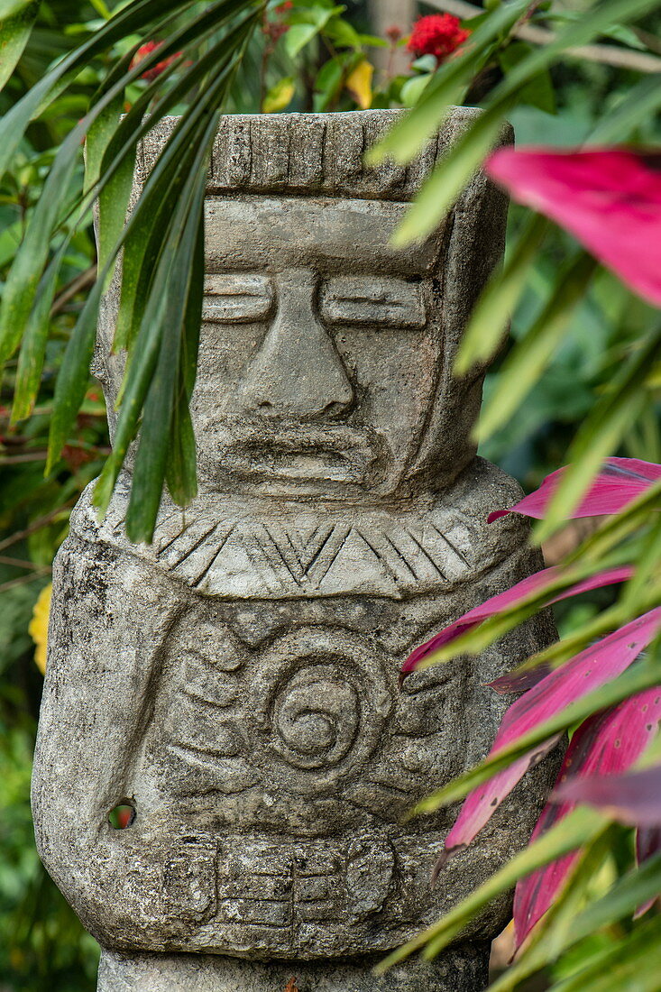 A stone figure representing a person is surrounded by palm fronds and leaves, Santa Marta, Magdalena, Colombia, Caribbean