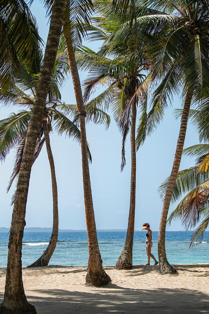 Eine Frau mit Sonnenschutz geht zwischen Kokospalmen entlang einem Strand, Isla Aroma, San Blas Inseln, Panama, Karibik