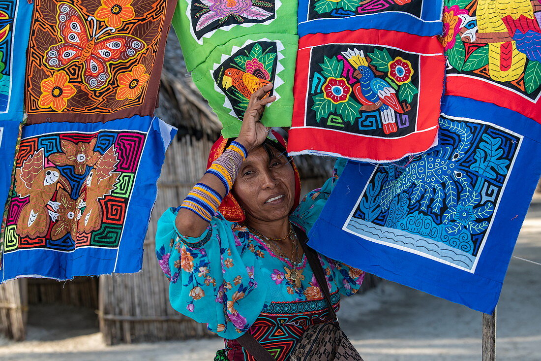 A Guna (formerly Kuna) native woman stands in front of colorful handmade Molas textiles that she sells to tourists, Isla Aroma, San Blas Islands, Panama, Caribbean