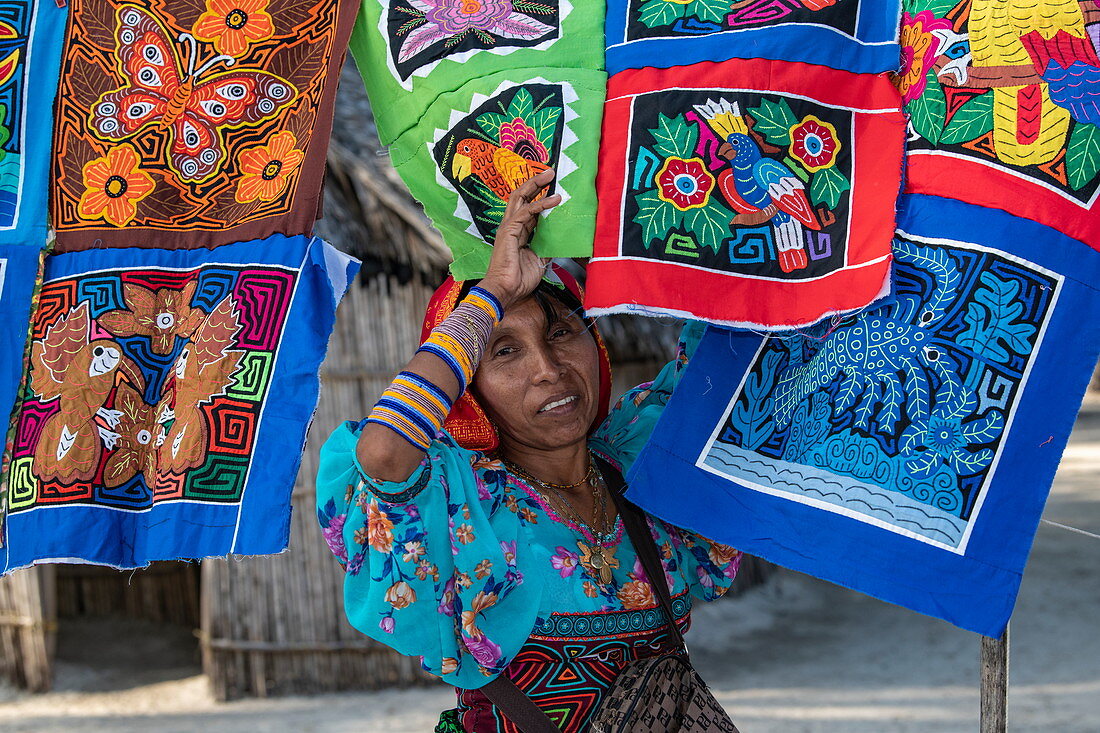 Eine Frau der Guna (ehemals Kuna) Ureinwohner steht vor farbenfrohen handgefertigten Molas Textilien, die sie an Touristen verkauft, Isla Aroma, San Blas Inseln, Panama, Karibik