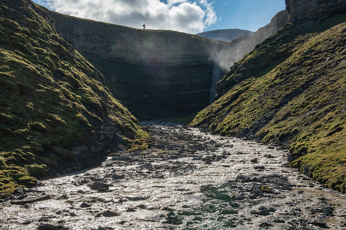 Fluss fließt von einem hohen Wasserfall zwischen steilen Hängen zum nur hundert Meter entfernten Ozean, Flintholmen, Spitzbergen, Norwegen, Europa