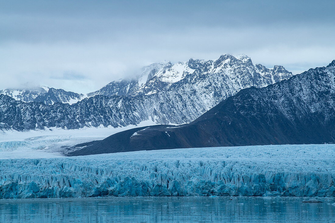 Grafische Szene von schroffen, schneebedeckten Bergen und einem breiten Gletscher, der sich bis zum Meer erstreckt, Lilliehöökfjord, Albert I. Land, Spitzbergen, Norwegen, Europa\n