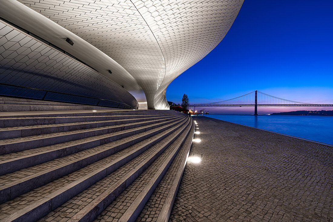 Kurz vor Sonnenaufgang auf den Stufen des MAAT (Museum) mit Blick auf den Tejo und die Ponte 25 de Abril in Lissabon, Portugal