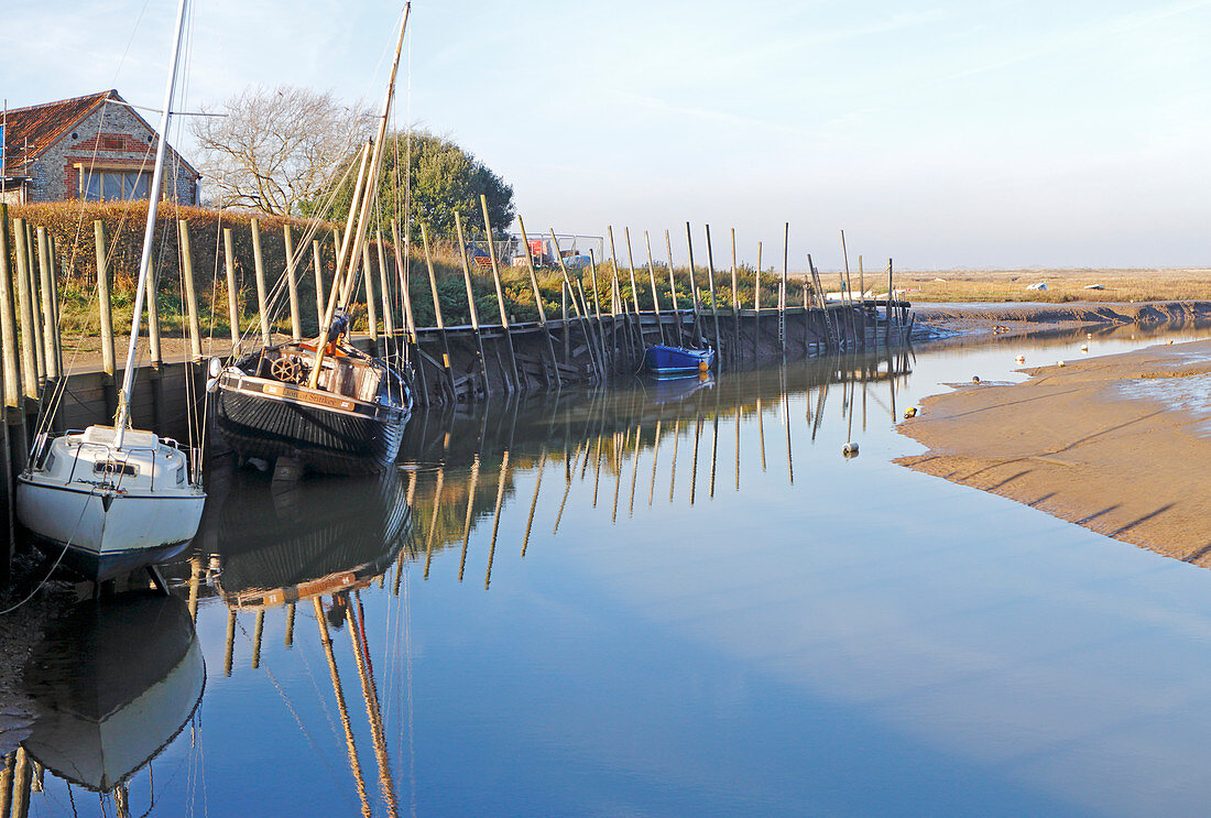 Blick auf den Kai und Liegeplätze am westlichen Ende des Hafens an der Küste von Nord-Norfolk bei Blakeney, Norfolk, England, Vereinigtes Königreich