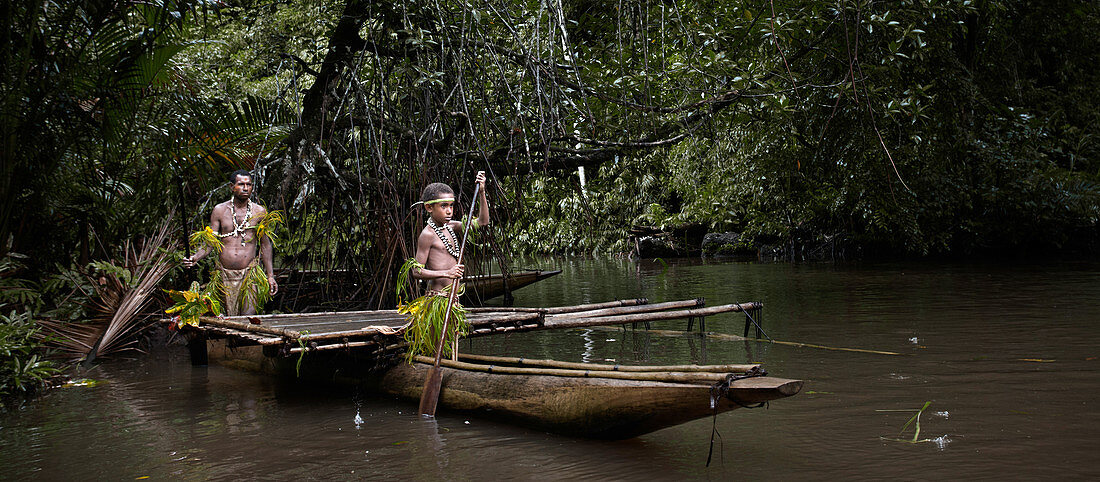 Papua New Guinea - November 8, 2010:  Father and son wearing traditional tribe clothing are rowing a boat in the jungle.