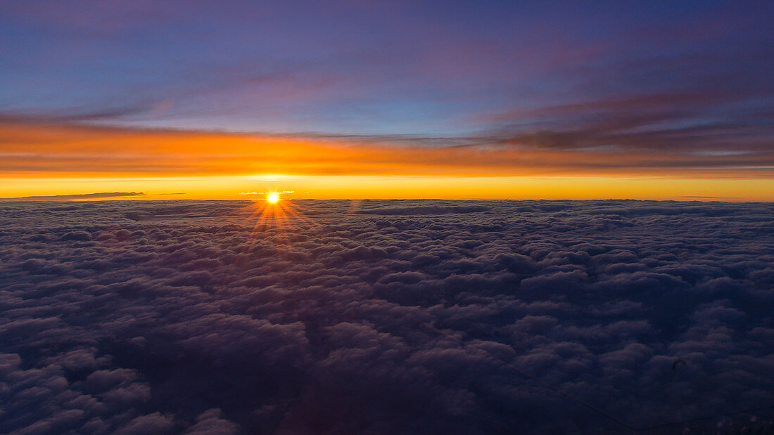 Sonnenuntergang über einer geschlossenen Wolkendecke, Luftbild aus dem Cockpit eines Airliners