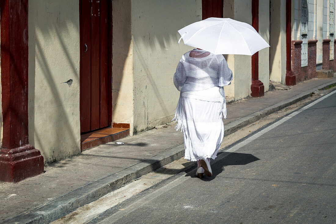 Frau mit weißem Sonnenschirm geht entlang der Straße, Camagüey, Kuba