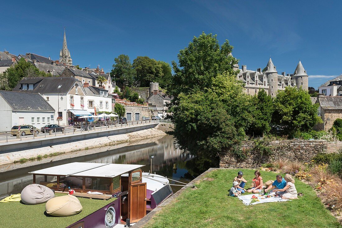 Frankreich, Morbihan, Josselin, Femilie beim Picknick am Kanal von Nantes nach Brest mit Blick auf die Burg von Rohan