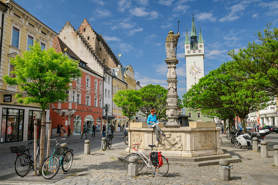 Frau beim Radfahren sitzt an Brunnen und liest, Stadtplatz Straubing, Straubing, Donau-Radweg, Niederbayern, Bayern, Deutschland