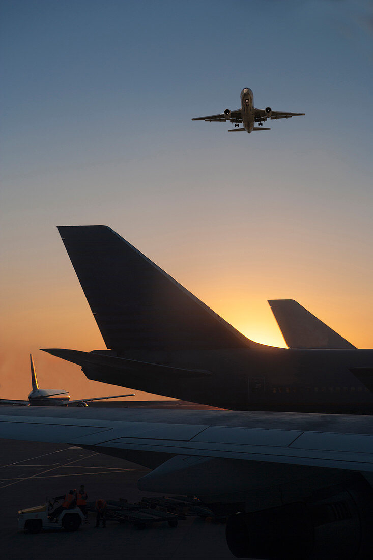 Flugzeug fliegt über Flugzeug auf Landebahn bei Sonnenuntergang