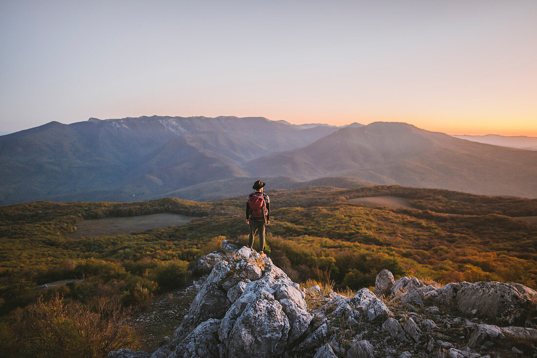 Man on rock by mountains at sunset