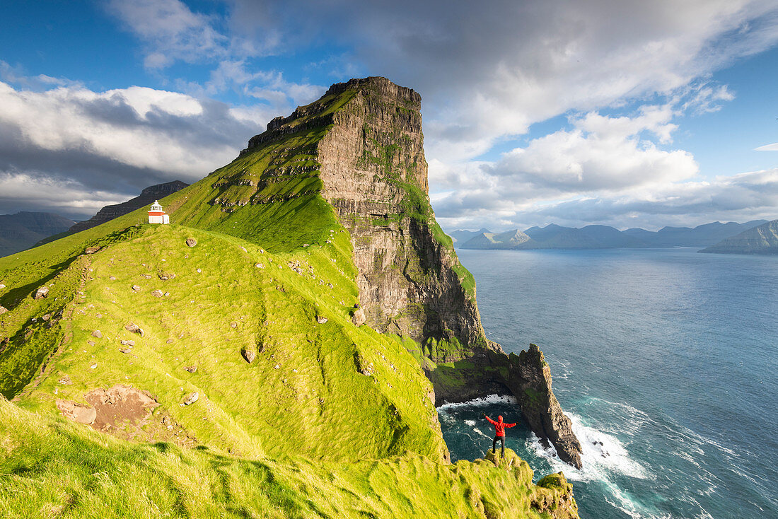 Hiker above the ocean towards Kallur lighthouse, Kalsoy island, Faroe Islands, Denmark