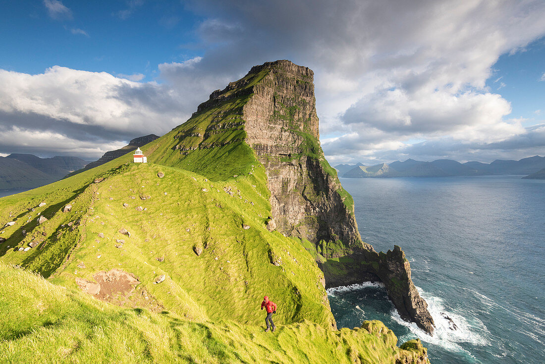 Hiker runs on steep cliffs at Kallur lighthouse, Kalsoy island, Faroe Islands, Denmark