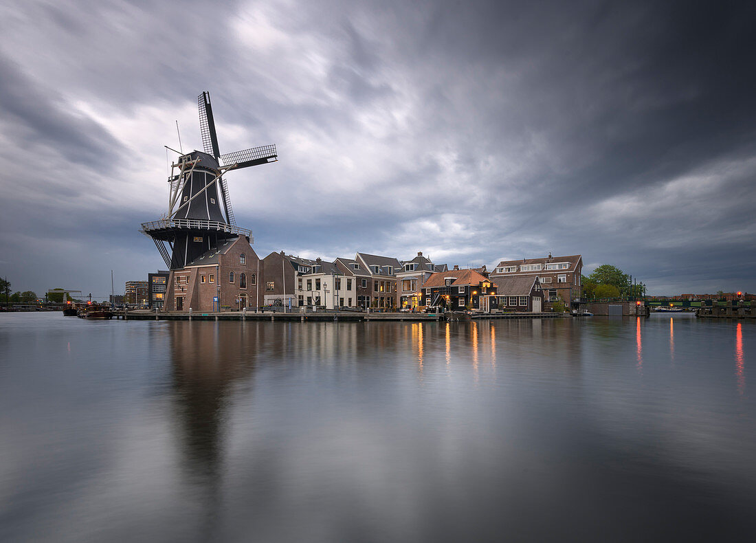 Blick auf die Windmühle De Adriaan, die sich während der Goldenen Stunde im Kanal des Flusses Spaarne spiegelt, Haarlem, Amsterdamer Bezirk, Papentorenvest, Randstad, Nordholland, Niederlande, Europa