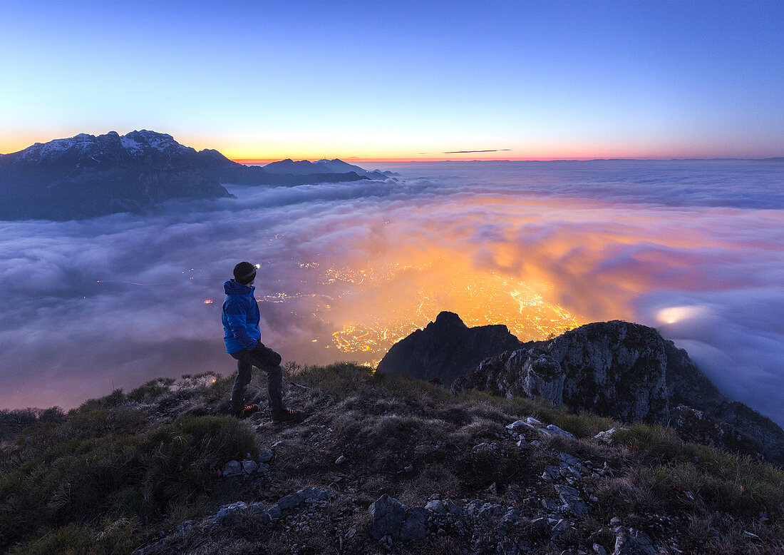 Hiker look the Lecco city wrapped of clouds from the top of Coltignone mount, Piani dei Resinelli, Lecco province, Lombardy, Italy, Europe (MR)