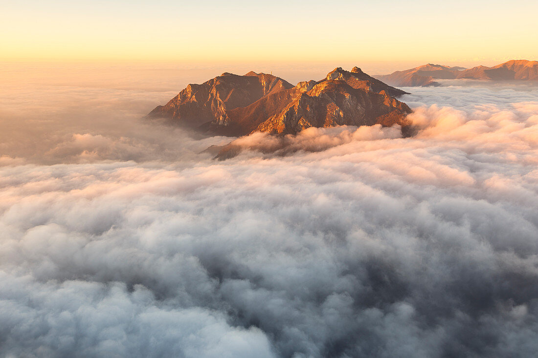 Sonnenaufgang über den Bergen von Lecco (Corni di Canzo, Rai, Moregallo), in Wolken gehüllt von der Spitze des Coltignone-Berges, Piani dei Resinelli, Provinz Lecco, Lombardei, Italien, Europa