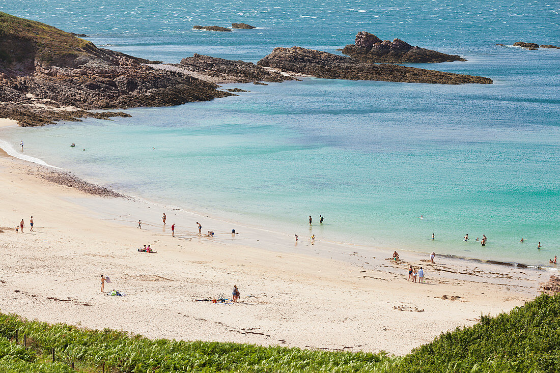 Summer on the beach below Cap Erquy in Brittany with bathing vacationers.