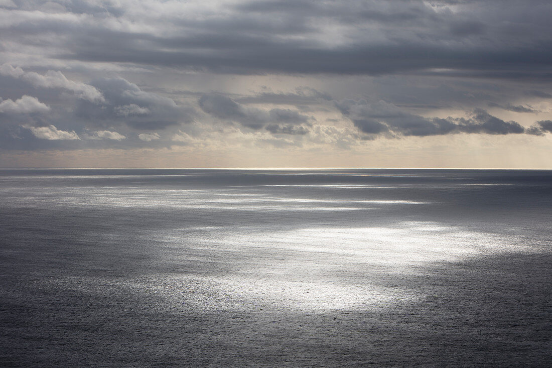 Storm clouds clearing over expansive ocean, dappled sunlight on water, northern Oregon coast