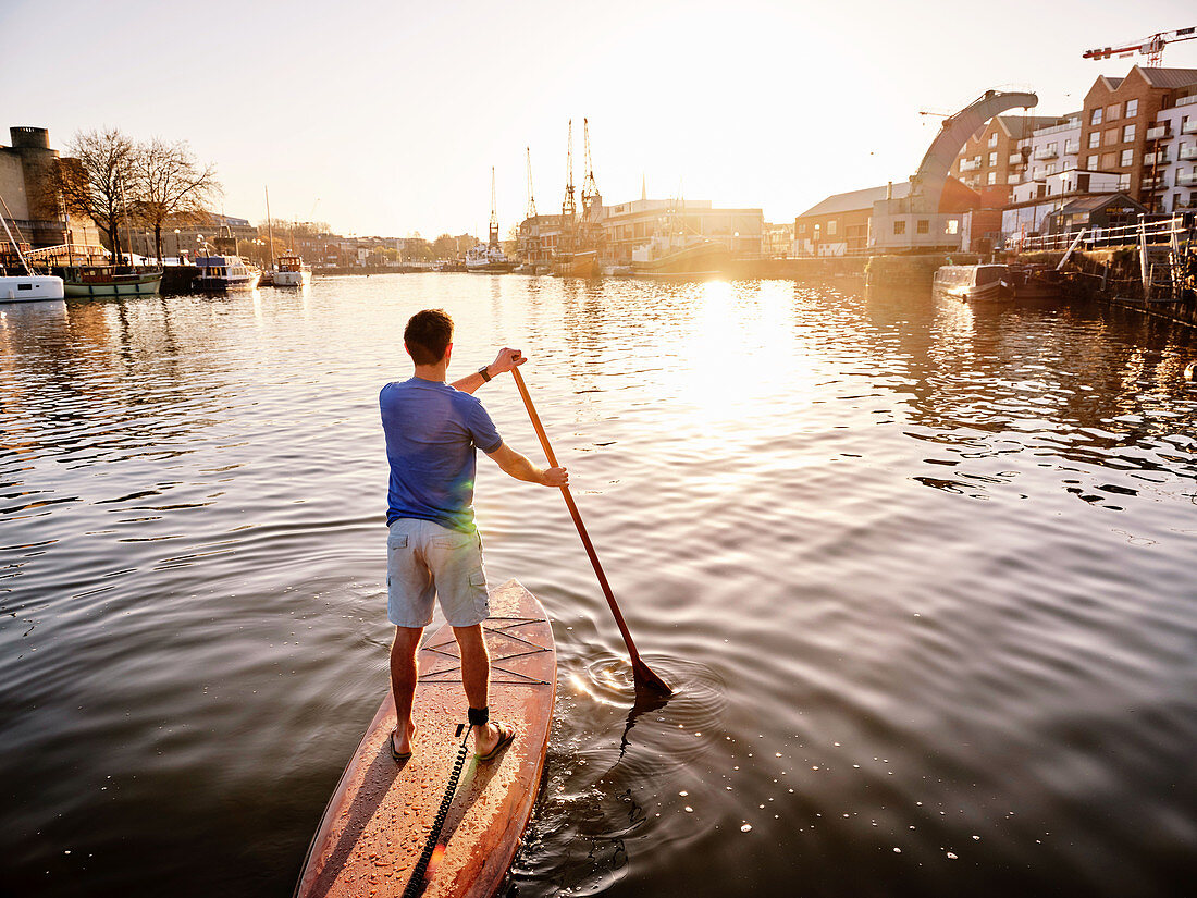 Mann steht auf einem Paddelboard auf dem Fluss im Morgengrauen, Rückansicht