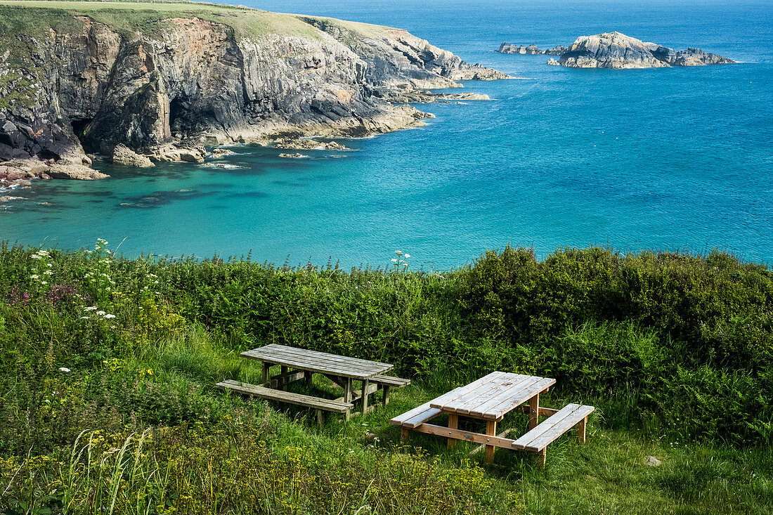 Picknicktische aus Holz auf einer Klippe an der Küste von Pembrokeshire, Wales, Großbritannien