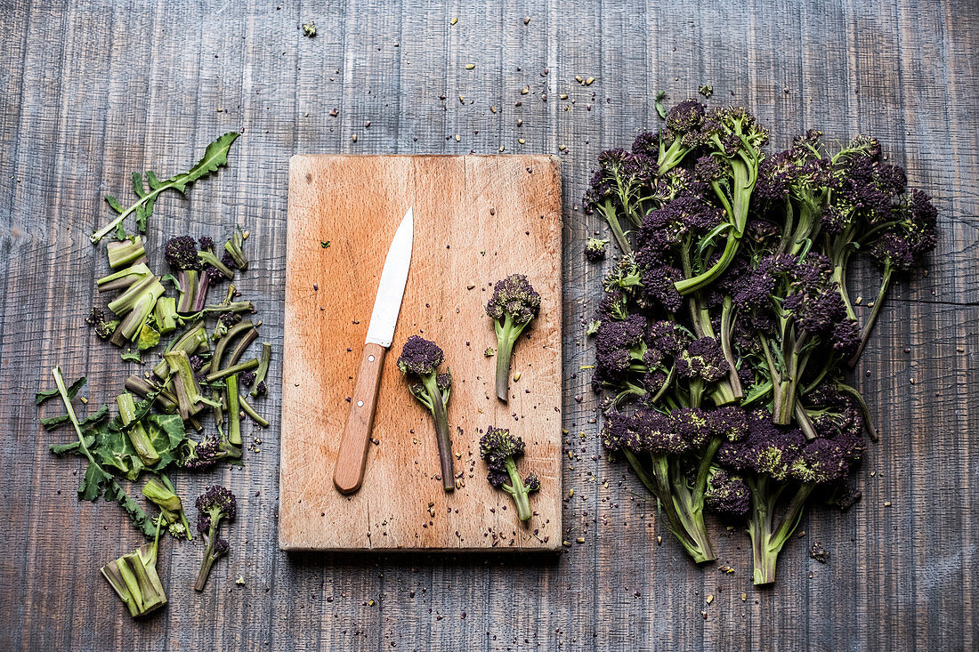 High angle close up of purple sprouting broccoli, knife and wooden cutting board.